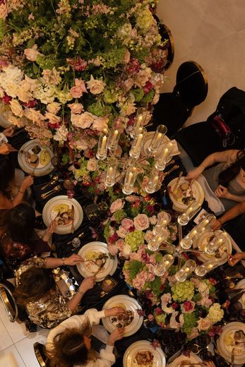 Guests gathered around a long floral-laden dinner table, seen from above
