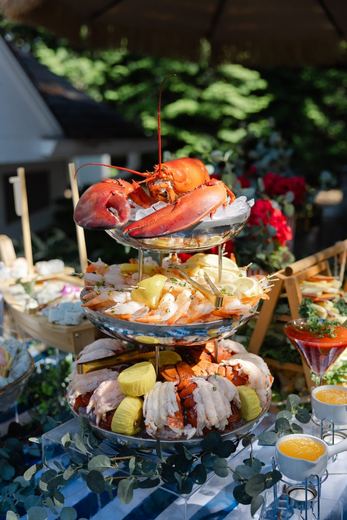 A tiered seafood tower of lobster and shrimp at an outdoor summer table